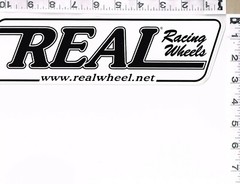 NEW, REAL RACING WHEELS STICKER, 11″ X 3″, BLACK WRITING ON WHITE BACKGROUND